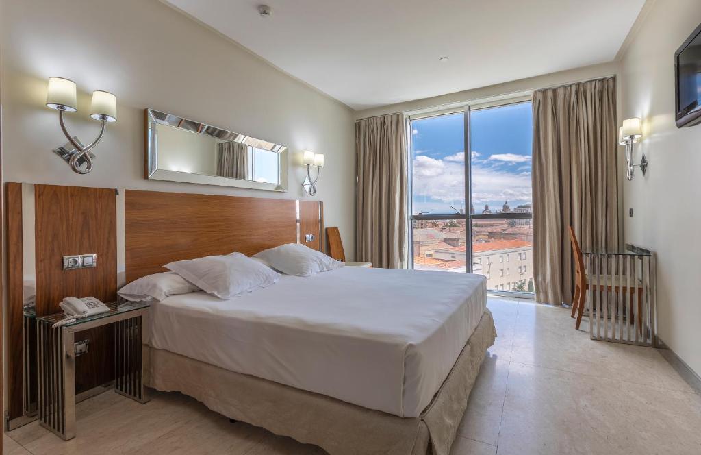 a hotel room with a bed and a large window at Gran Hotel Corona Sol in Salamanca