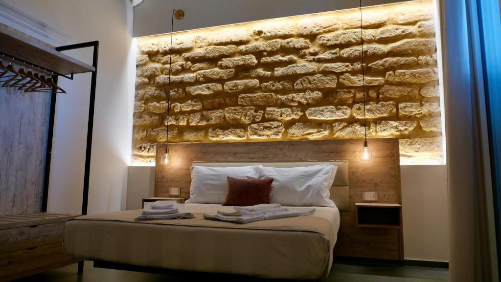 1 dormitorio con una pared de piedra sobre una cama en Oneira Rooms, en Agrigento