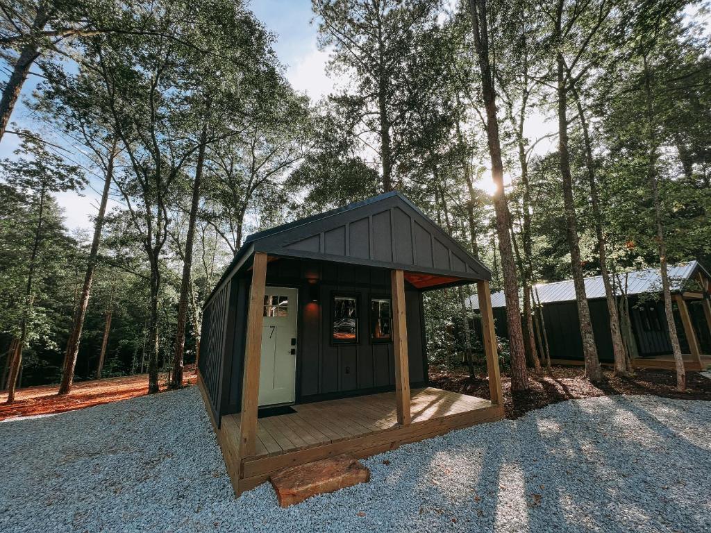 a small black house with a deck in the woods at Cabin #7 With Kitchenette in Hartwell