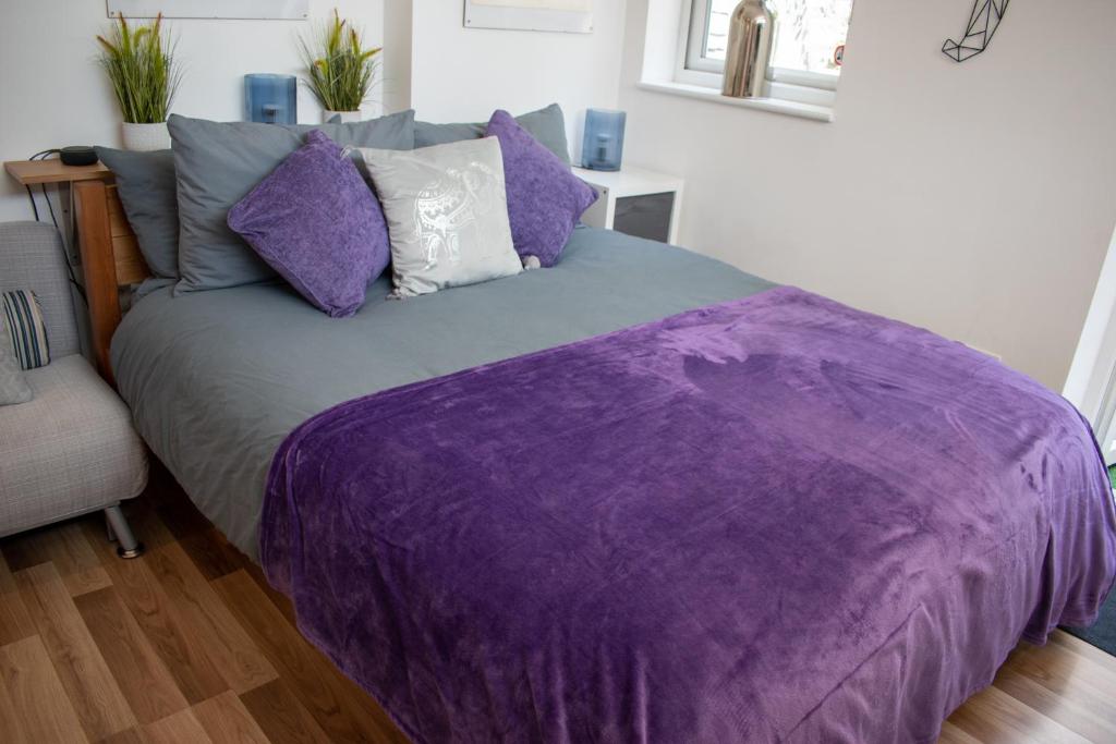 a bed with a purple comforter in a room at 121 Studio - Central Studio Apartment, Terrace & Full Kitchen - Airport & Train Shuttle in Bishops Stortford