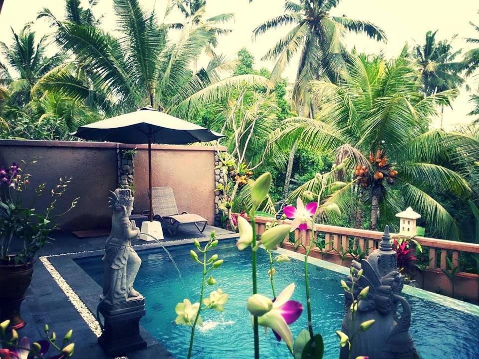 a pool with an umbrella and some palm trees at Villa Cilinaya Ubud in Ubud