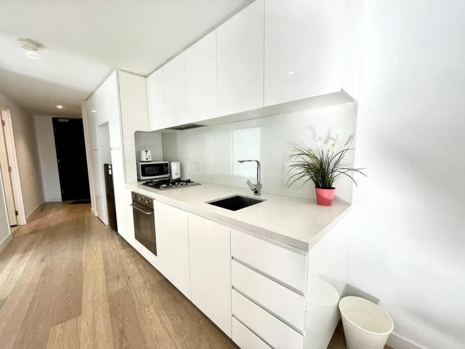 a white kitchen with a sink and a microwave at 1 Bedroom Modern Apartment Near Crown and CBD in Melbourne