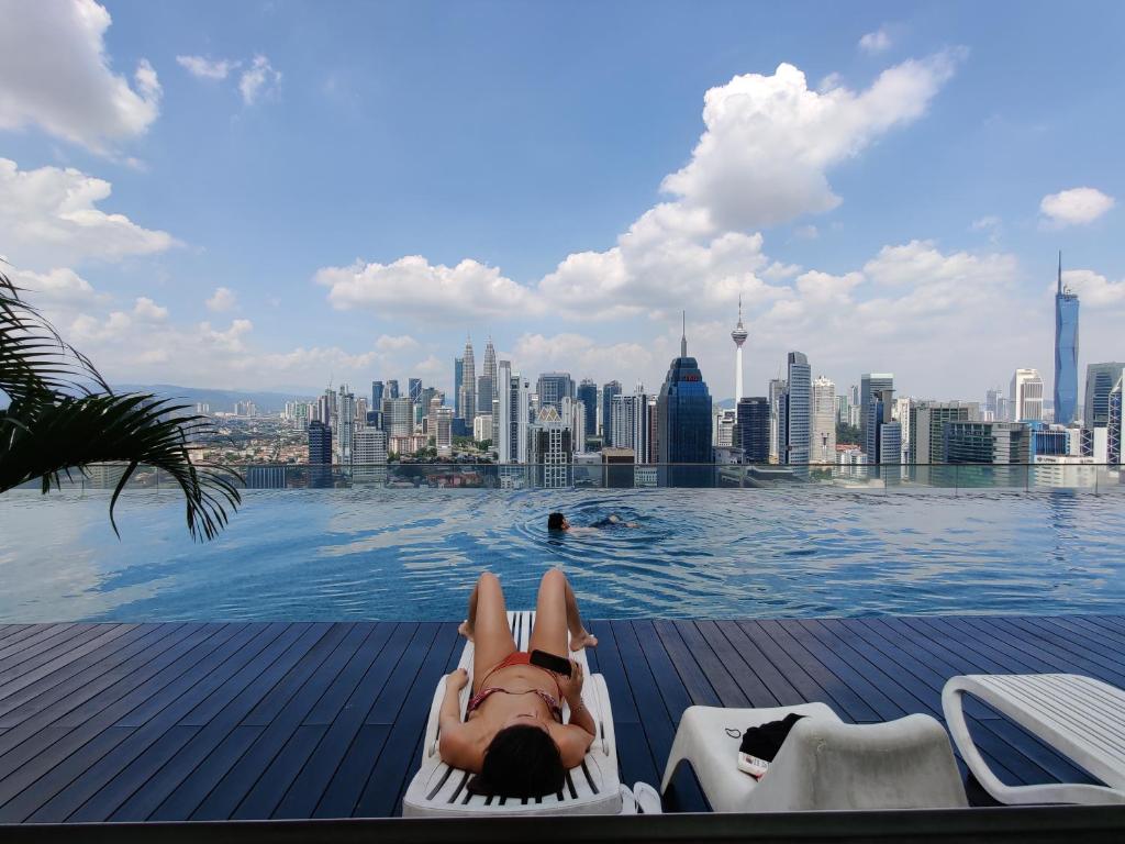 a woman laying on the edge of a pool with a city skyline at StarsBed KLCC Skyview Roof Pool Hostel in Kuala Lumpur