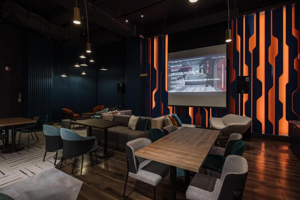 a restaurant with tables and chairs and a projection screen at OLAH Poshtel - Taichung Station in Taichung