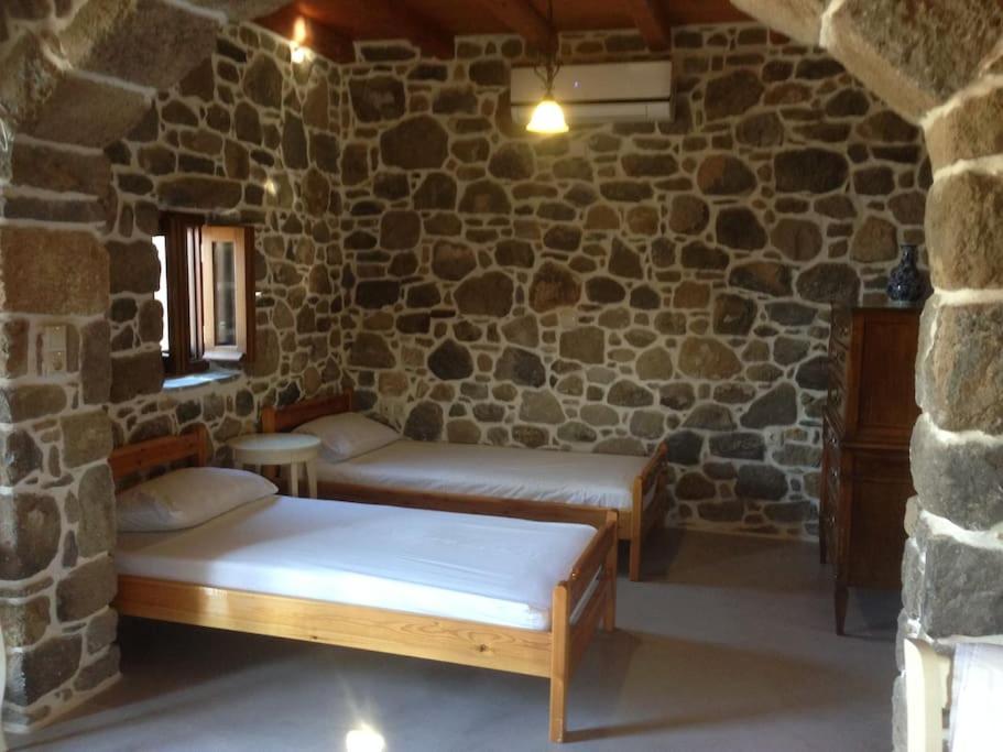 a room with two beds in a stone wall at Loutra Olive Garden Stone House #3 in Mandrakion