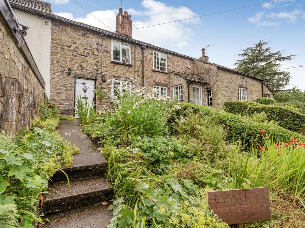 una vieja casa de ladrillo con un jardín delante de ella en Fox Bank Cottage, en Macclesfield