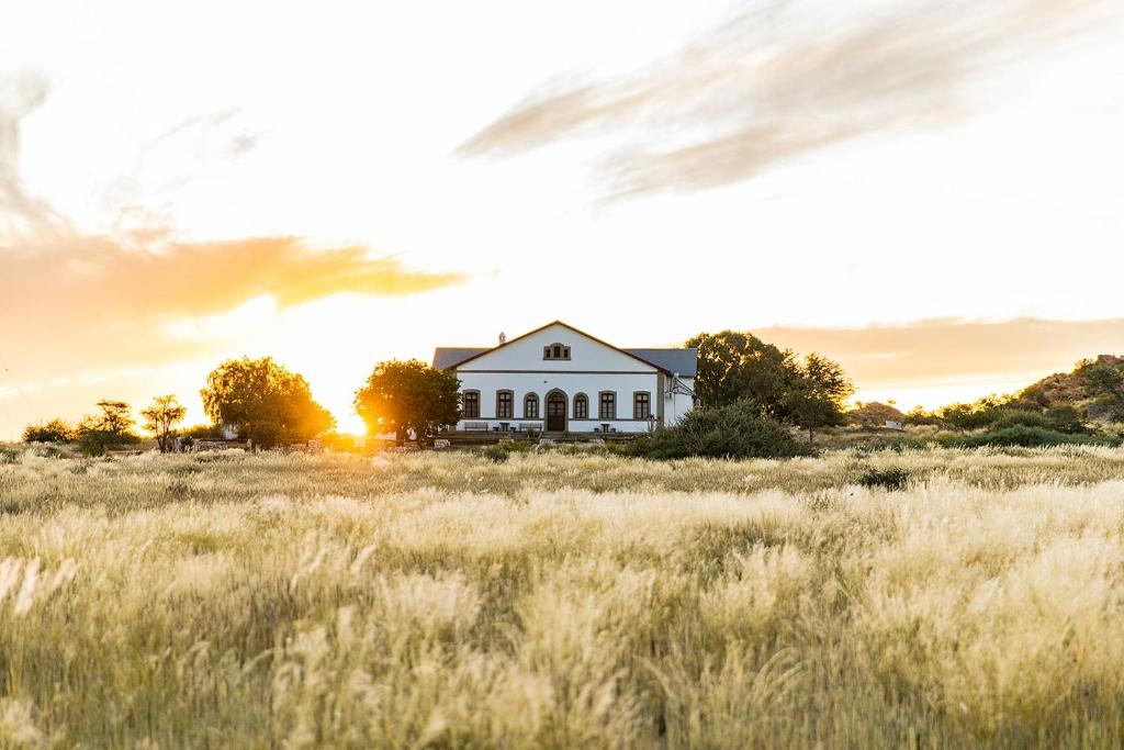 uma casa num campo com o pôr do sol atrás dela em White House Guest Farm em Grünau