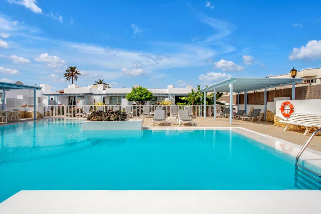 a large blue swimming pool with chairs and a building at Mar Azul Corralejo- Adults Only in Corralejo