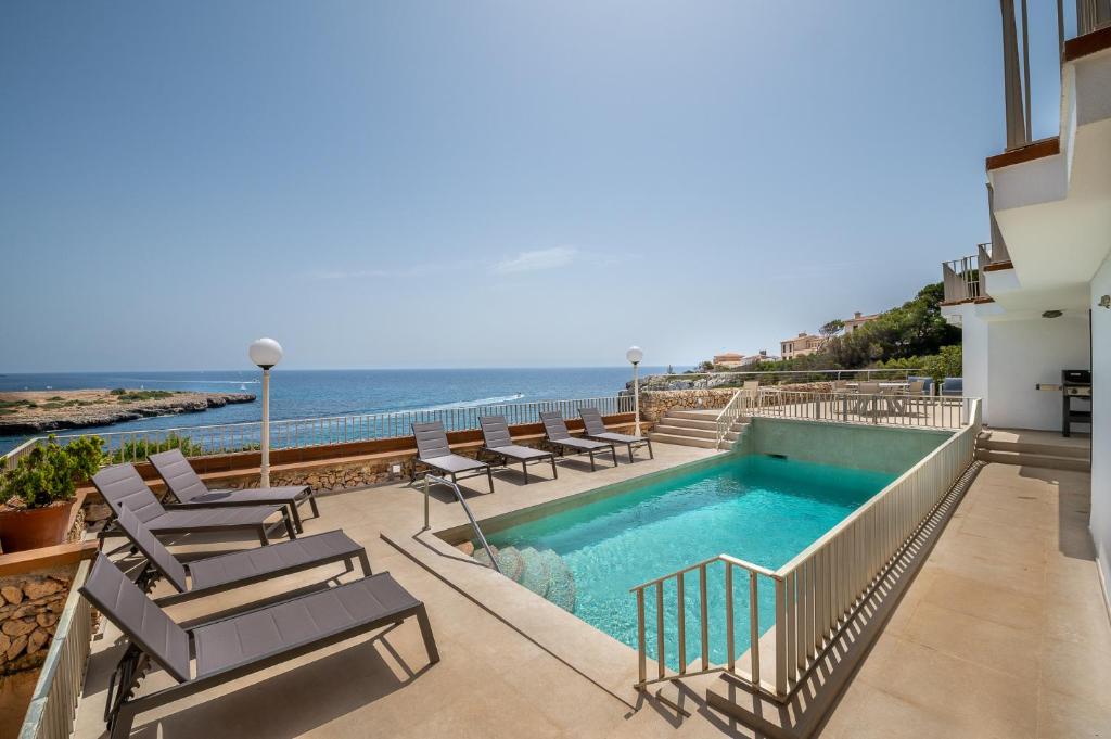a swimming pool with chairs and the ocean in the background at Villa Enderrossall in Porto Cristo