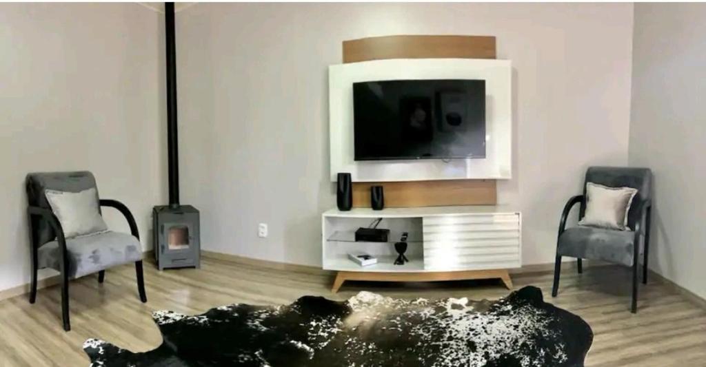 a living room with two chairs and a flat screen tv at Casa 21, aconchegante com lareira in Bento Gonçalves