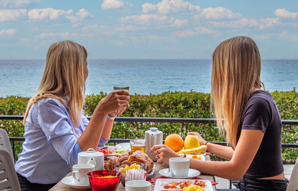 two women sitting at a table with food and the ocean at Best Western Premier Hotel Prince de Galles in Menton