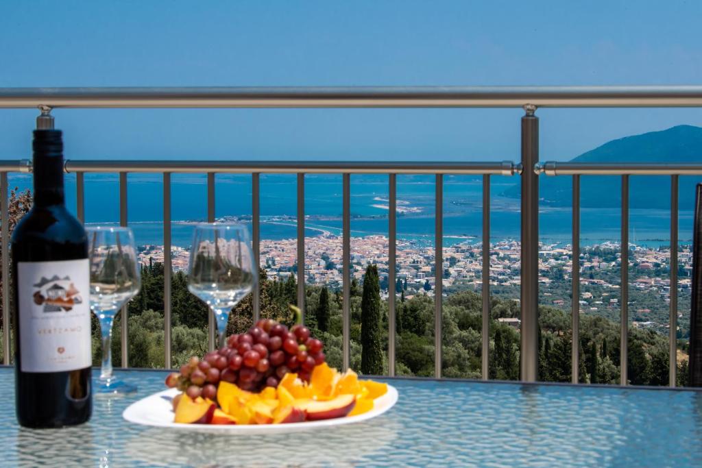 Villelia View Villas 2 في Apolpaina: صحن من الفاكهة وكؤوس النبيذ على طاولة مطلة