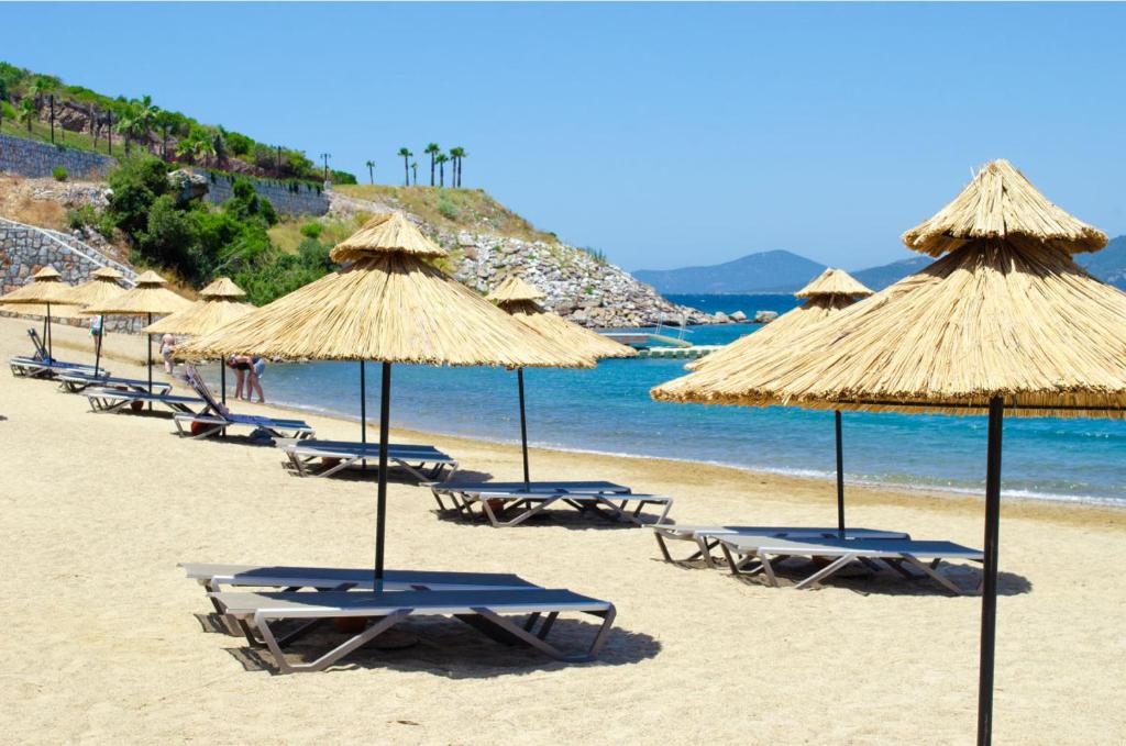 a group of beach chairs with straw umbrellas on a beach at Castamar Residence in Bodrum City