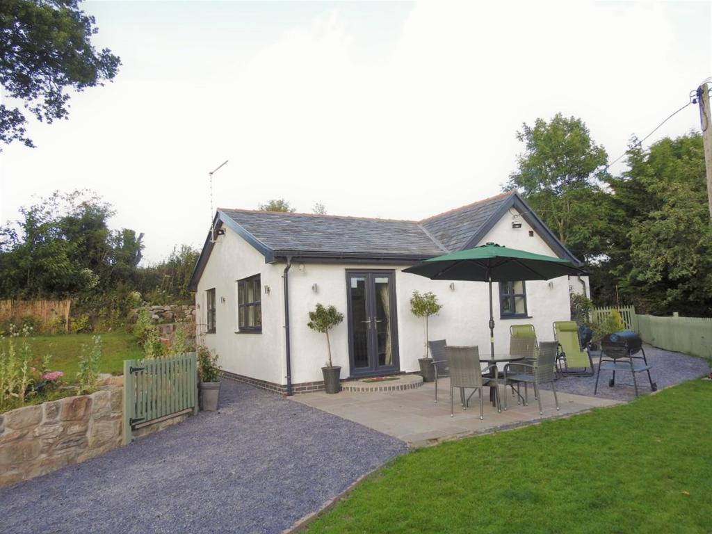 une petite maison blanche avec une table et un parasol dans l'établissement Cosy country cottage with outdoor bathing, à Halkyn