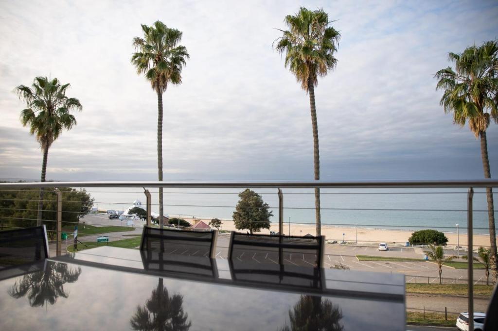 uma varanda com vista para a praia e para as palmeiras em Santos Seaview Apartment em Mossel Bay