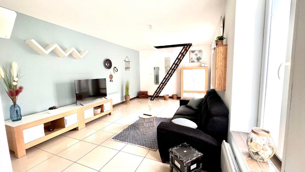 ein Wohnzimmer mit einem schwarzen Sofa und einem TV in der Unterkunft Agréable maison de ville cosy de 122m² + extérieur in Wattrelos