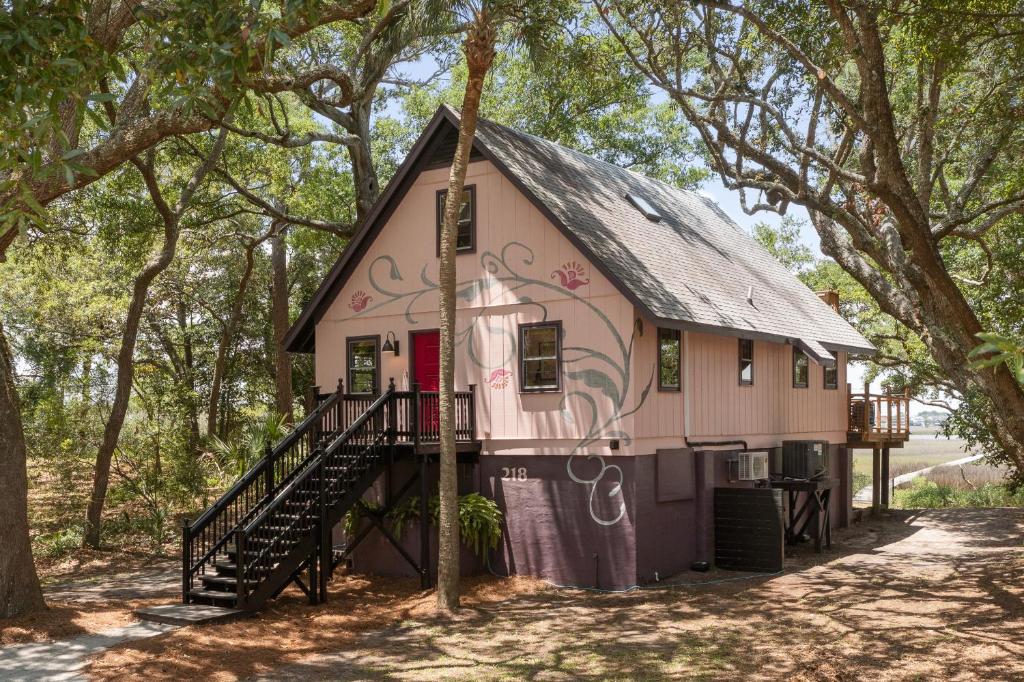 ein rosa Haus mit schwarzem Dach im Wald in der Unterkunft Folly Vacation Vintage Cottage with Stunning Views 218 in Folly Beach