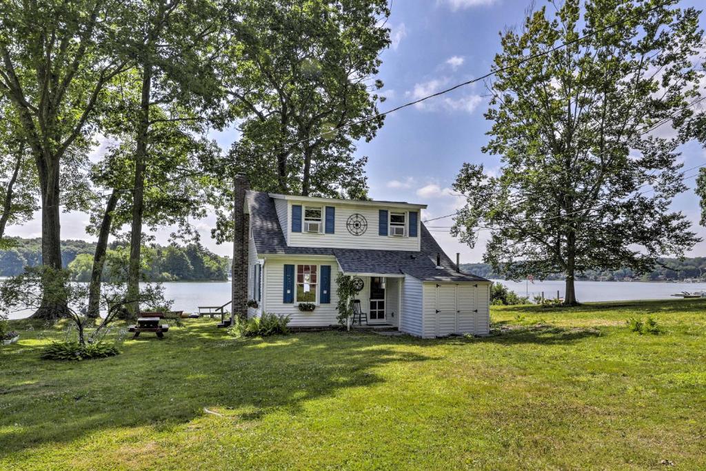 a small white house on a lawn with a lake at Lakefront Cottage with Covered Porch and Dock! in Coventry