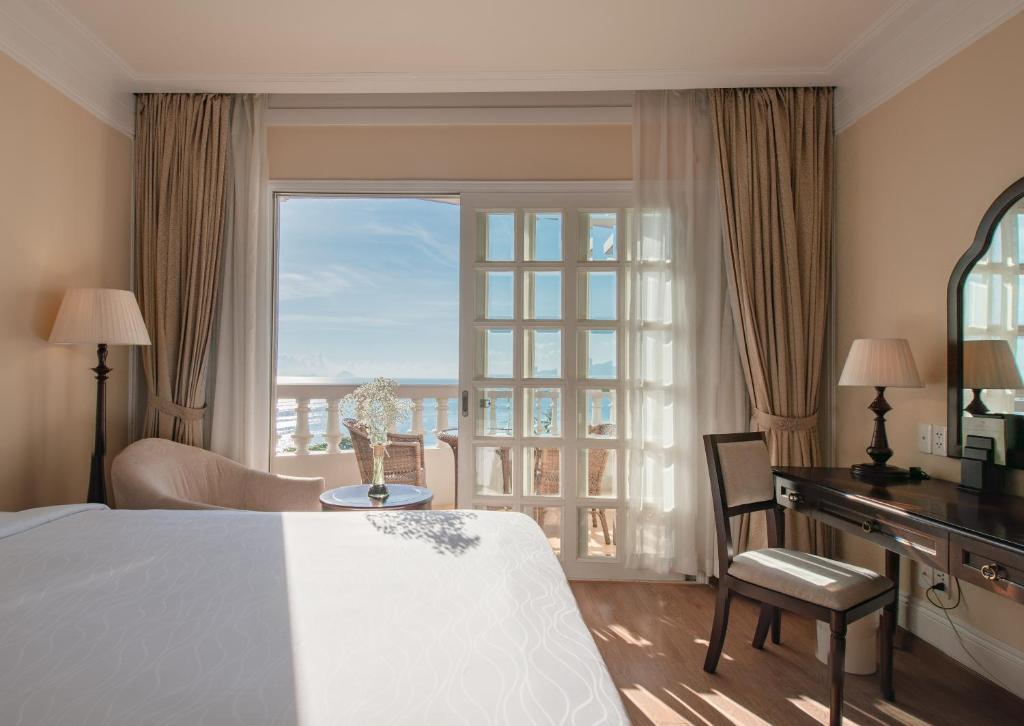 ニャチャンにあるサンライズ ビーチ ホテル & スパ ニャ チャンのベッド、デスク、窓が備わるホテルルームです。