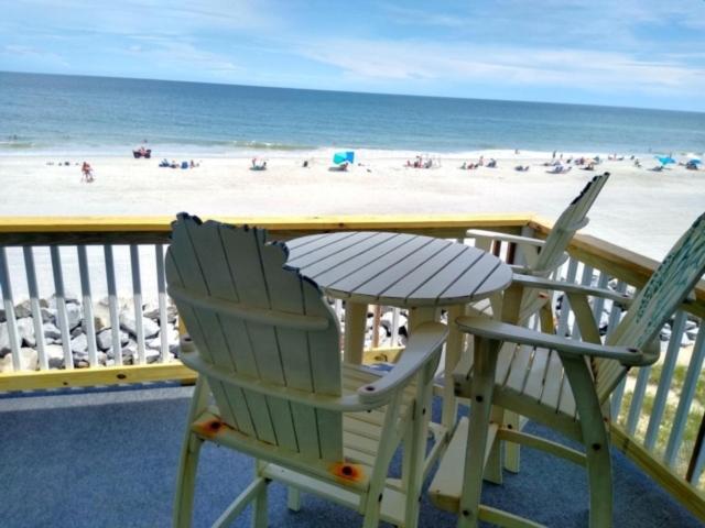 two chairs and a table on a balcony overlooking the beach at A18 Parrot Escape - OCEAN VIEW! There is nothing quite like a Carolina sunrise viewed from your private oceanfront deck condo in Carolina Beach