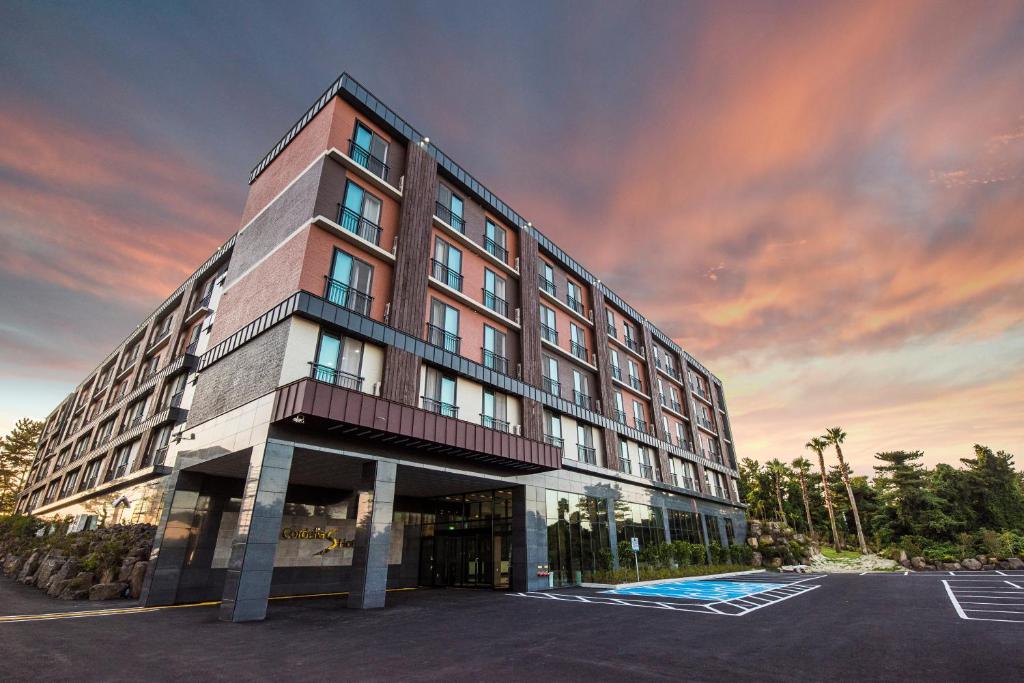 a building in a parking lot with a sunset at Cordelia Hotel in Seogwipo