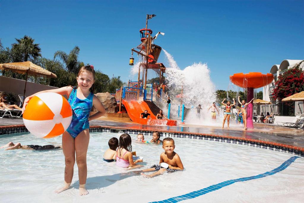 una chica sosteniendo una pelota de playa en una piscina en un parque acuático en Howard Johnson by Wyndham Anaheim Hotel & Water Playground, en Anaheim