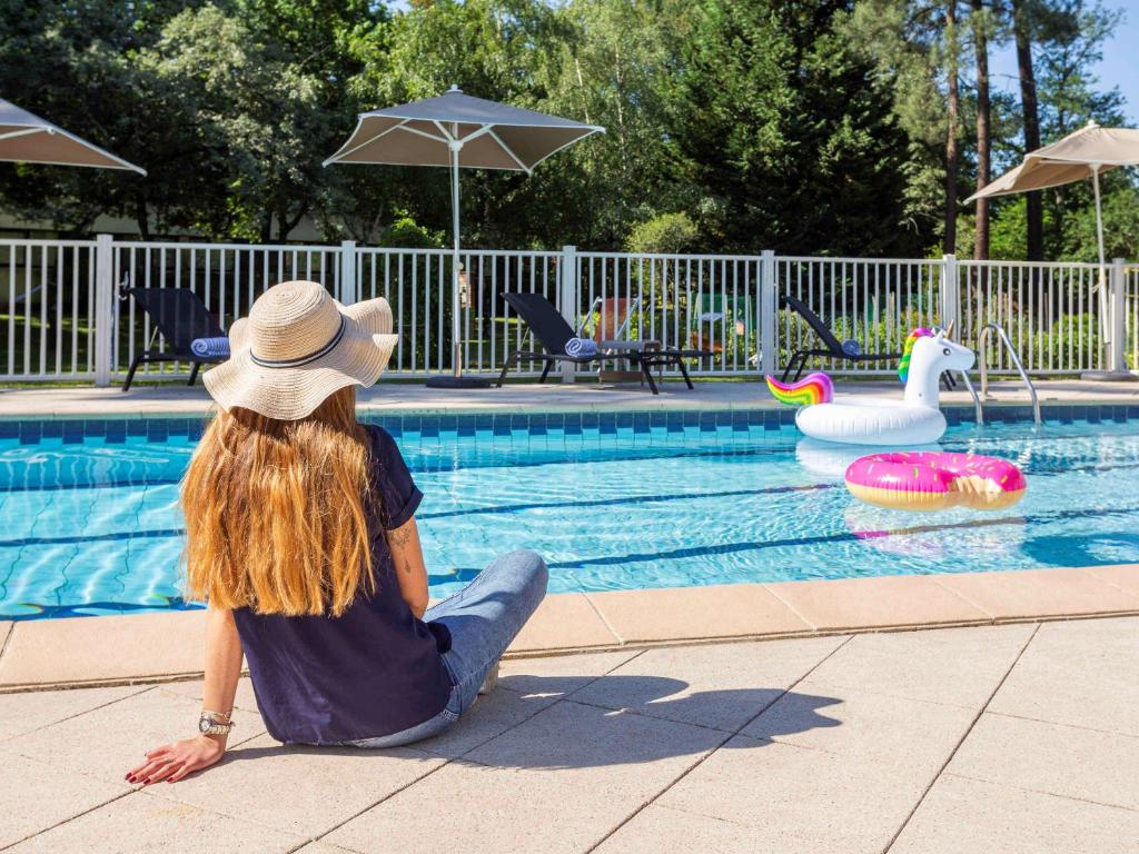 uma mulher sentada ao lado de uma piscina em Novotel Bordeaux Mérignac em Mérignac