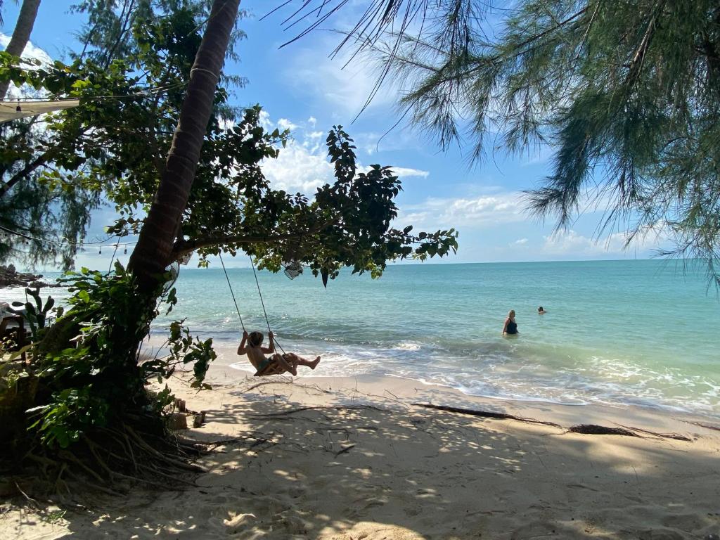 a swing on a beach with people in the water at Secret Beach Bungalows in Haad Son