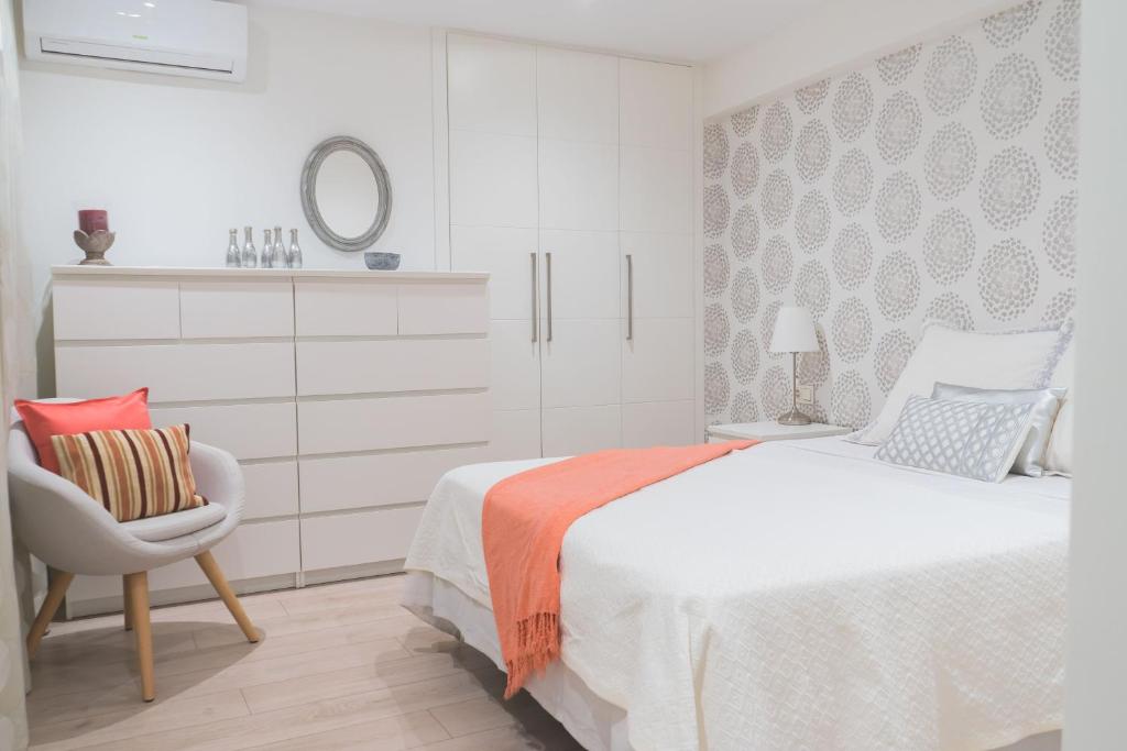 ein weißes Schlafzimmer mit einem Bett und einem Stuhl in der Unterkunft Precioso Apartamento 2 hab. en Malaga Centro in Málaga