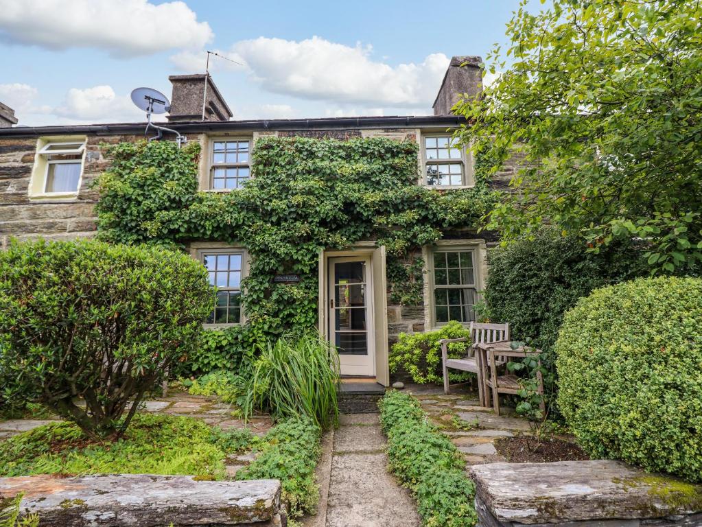 une maison recouverte de lierre avec une porte blanche et un banc dans l'établissement Preswylfa, à Blaenau Ffestiniog