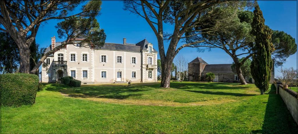 Une grande maison blanche avec des arbres dans la cour dans l'établissement Vignoble Château Piéguë - winery, à Rochefort-sur-Loire
