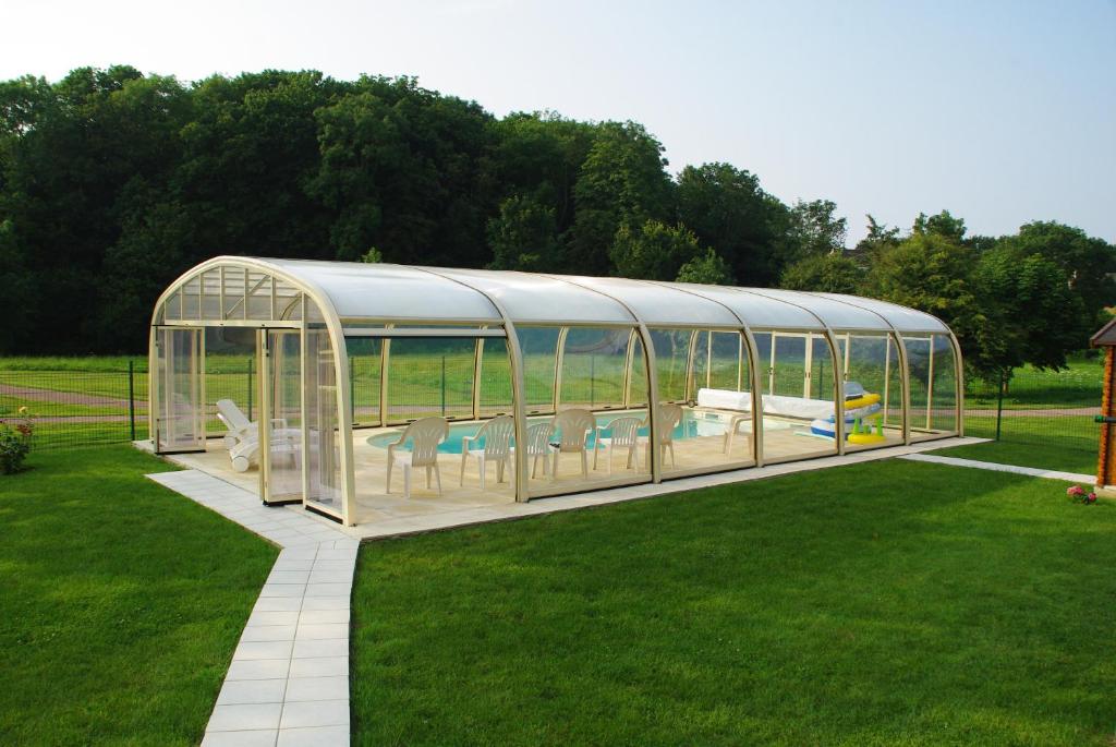 a glass greenhouse with a pool in a yard at La Grimodière Chambre en rez de chaussée in Ranville