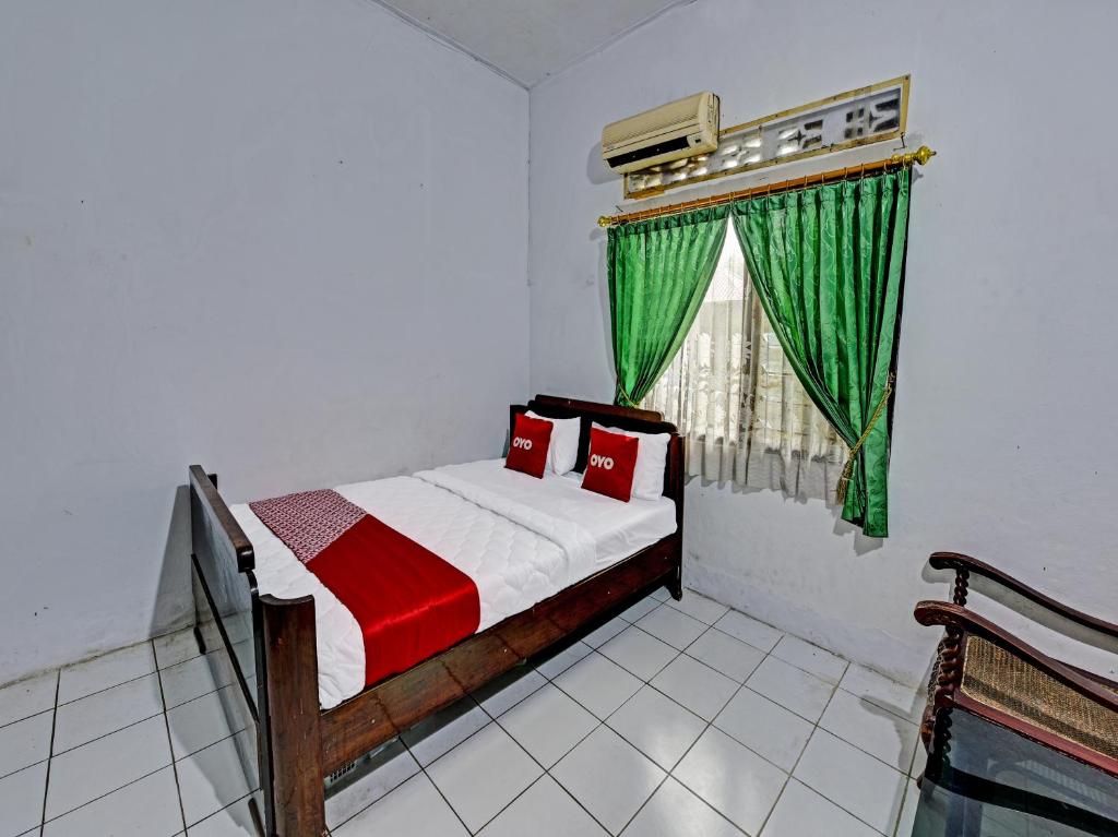a bedroom with a bed and a window with green curtains at SPOT ON 91372 Wisma Bulin in Purwokerto