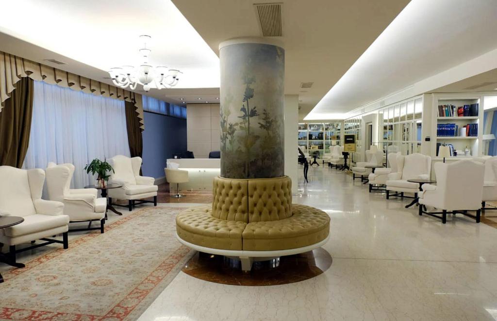 a lobby with white chairs and a column in the middle at Hotel Roxy Plaza in Soave