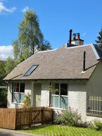 una pequeña casa blanca con una valla de madera en Cobbler's Cottage at Kindrochet, Strathtay en Pitlochry