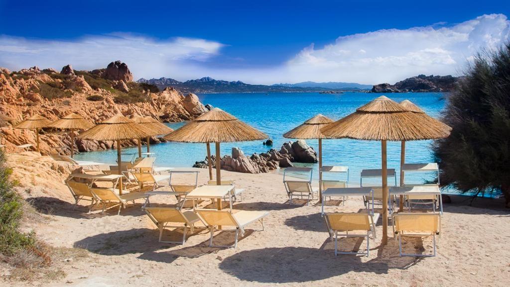 un grupo de sillas y sombrillas en una playa en Hotel Cala Lunga, en La Maddalena