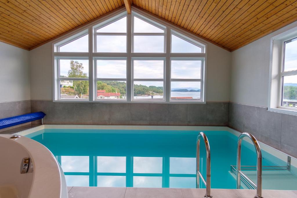 a large swimming pool with blue water in a room with windows at Exclusive fjordside villa with swimming pool, sauna, jacuzzi and boat hire in Sveio