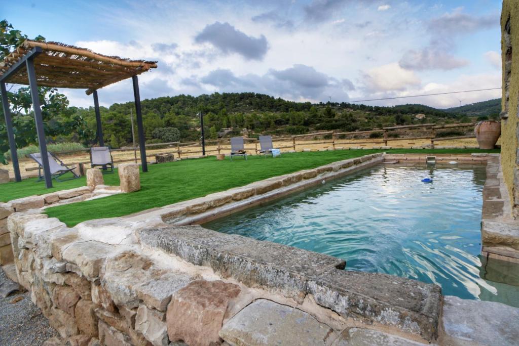 una piscina al aire libre con una pared de piedra y una pérgola en Serra de Martines en Batea
