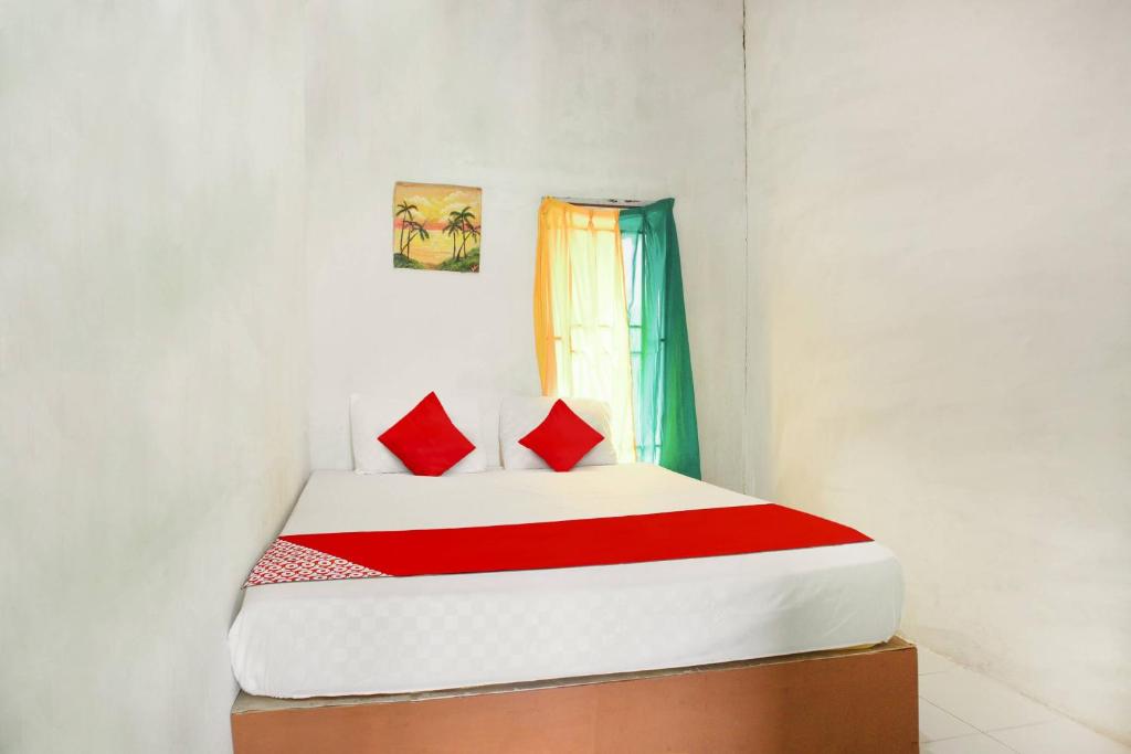 a bedroom with a bed with red pillows and a window at OYO 91051 Penginapan Pondok Ratu 354 in Pontianak