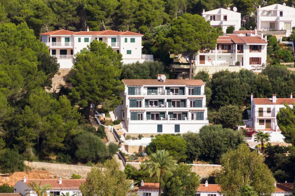 a large white house on a hill with houses at Apartamentos Encanto Del Mar in Cala Galdana