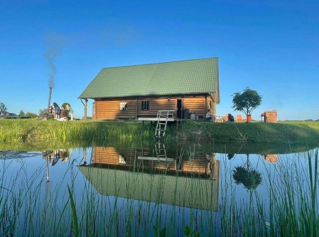 una cabaña de madera con su reflejo en el agua en Zaķu muiža en Anspoki