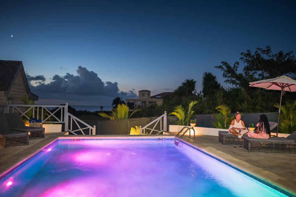 two people sitting on chairs next to a swimming pool at night at West Rock Villas in Saint James