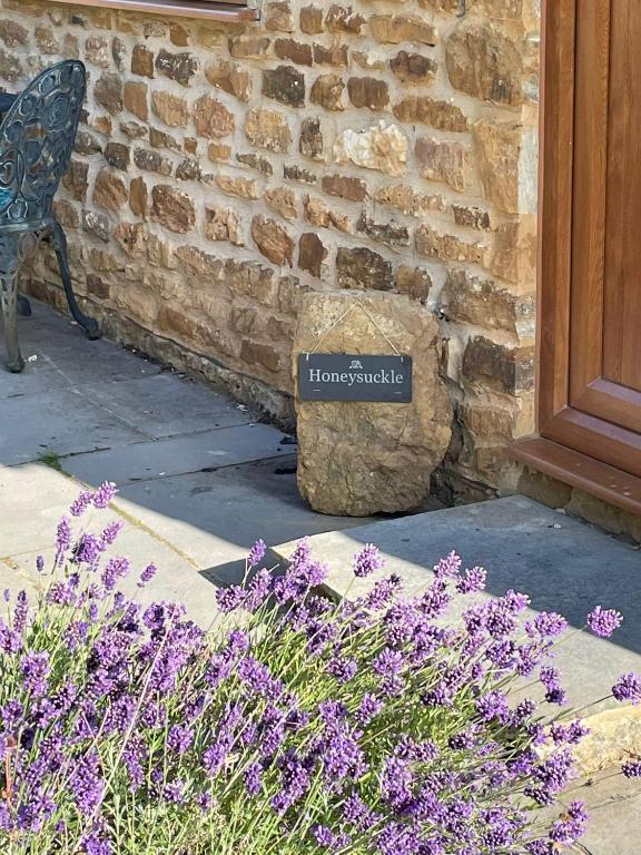 a sign in front of a brick building with purple flowers at Honeysuckle Cottage - Hillside Holiday Cottages, Cotswolds in Warmington