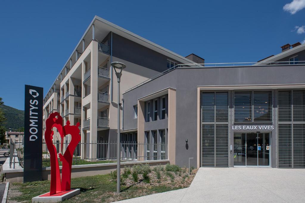 un edificio con una scultura rossa di fronte di Résidence services seniors DOMITYS LES EAUX VIVES a Digne-Les-Bains