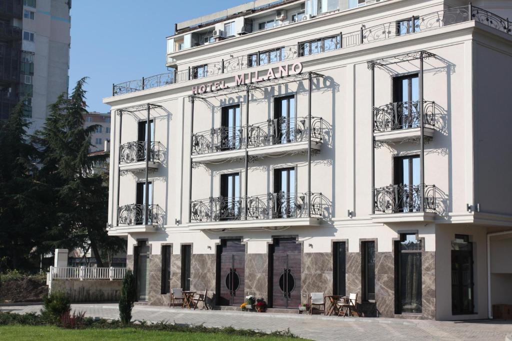 a white building with balconies and tables in front of it at Milano Hotel in Burgas