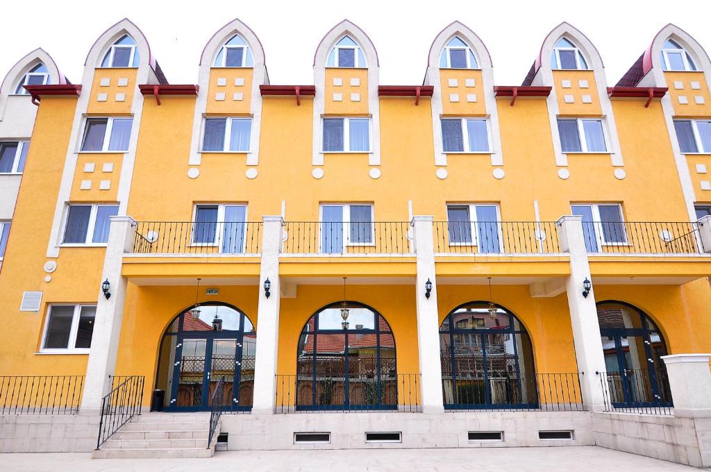 Edificio amarillo con ventanas arqueadas y balcón en Hotel Maxim, en Oradea
