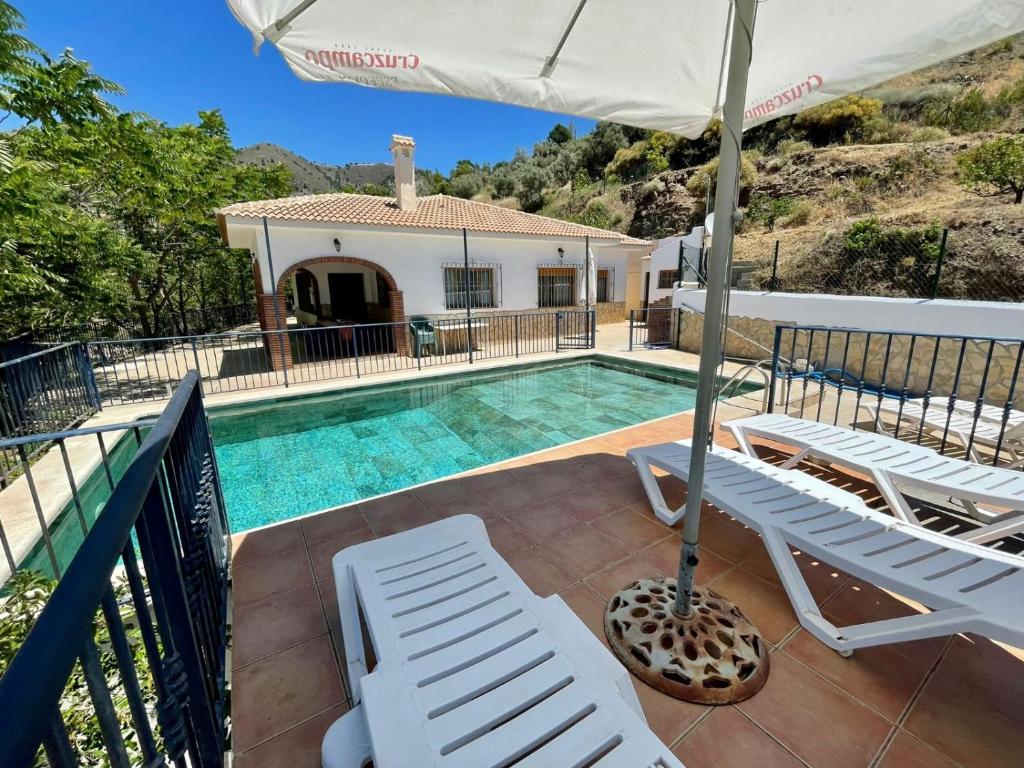 a villa with a swimming pool with chairs and an umbrella at FINCA EL ALMENDRO in Málaga