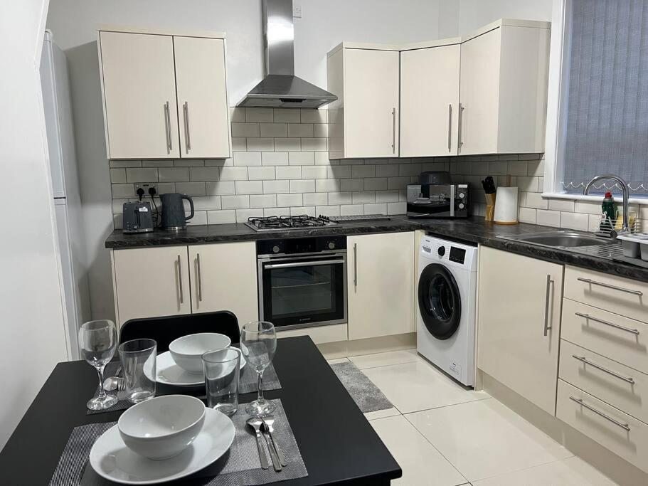 a kitchen with white cabinets and a table with dishes on it at Comfortably furnished 2 bedroom home in Bolton in Bolton