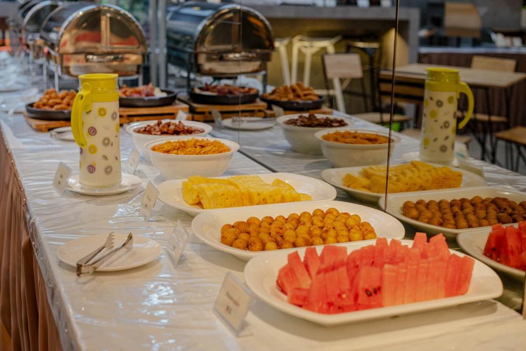 A buffet counter displaying fruit, pastries, hot dishes, and serving utensils.
