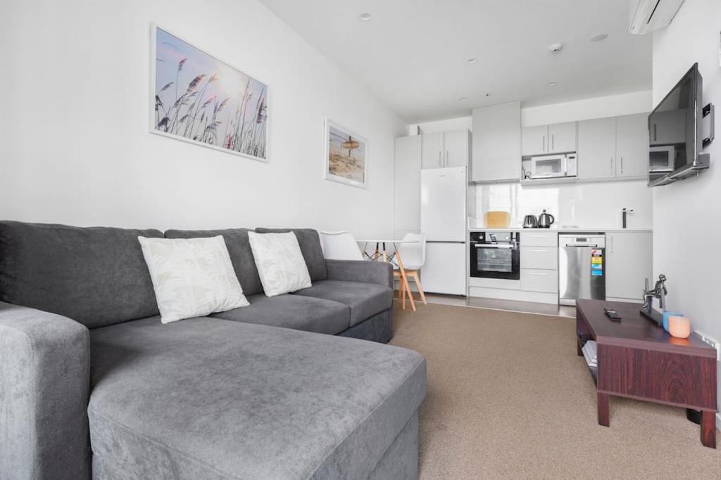 Il comprend un salon avec un canapé gris et une cuisine. dans l'établissement Cool Ra-mada Hideaway with air-con and deck, à Auckland